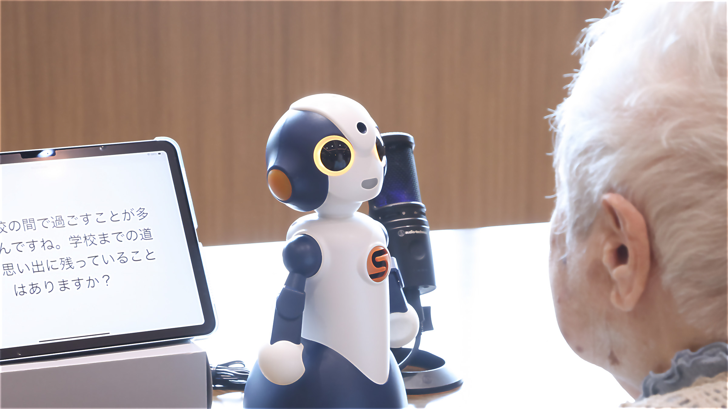 対話ロボットがタブレットに質問を表示し、入居者に思い出を問いかける様子
